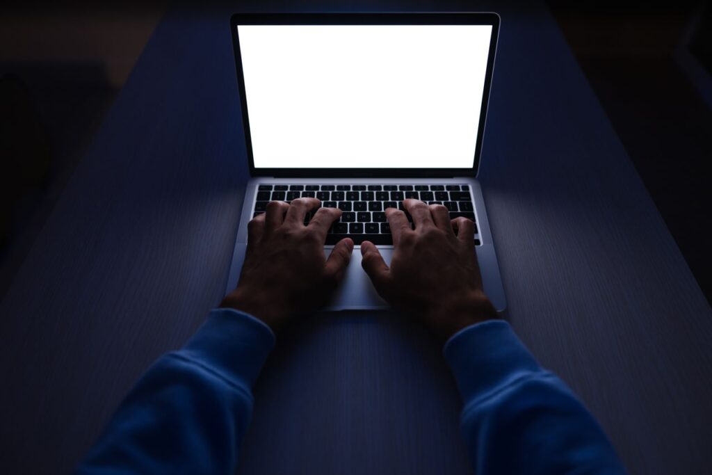 Hands typing on a laptop in a dark room, the kind of late-night remote work ai training platforms advertise