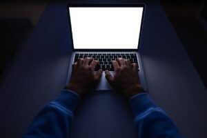 Hands typing on a laptop in a dark room, the kind of late-night remote work AI training platforms advertise