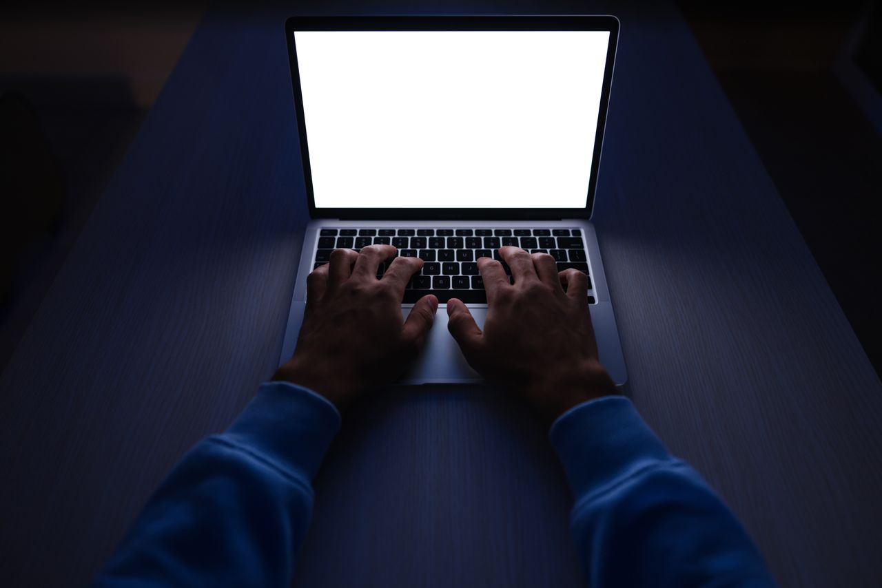 Hands typing on a laptop in a dark room, the kind of late-night remote work AI training platforms advertise
