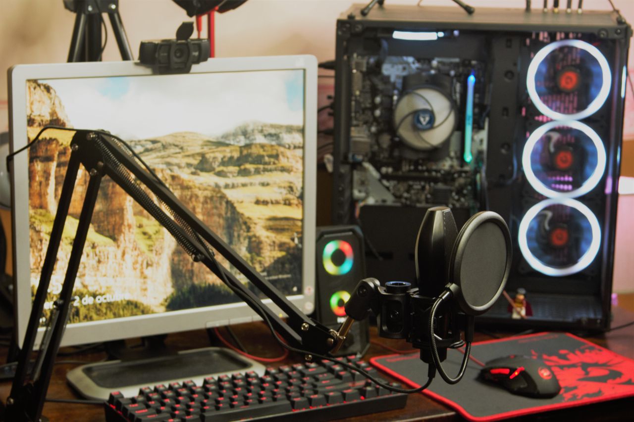 Condenser microphone on a boom arm in front of a keyboard, monitor and gaming PC on a home desk